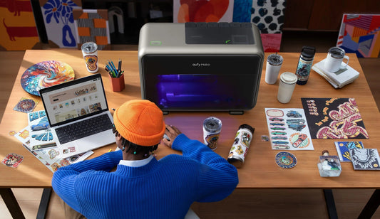A person designs custom prints on a laptop beside an active eufyMake E1 UV printer and colorful printed crafts.