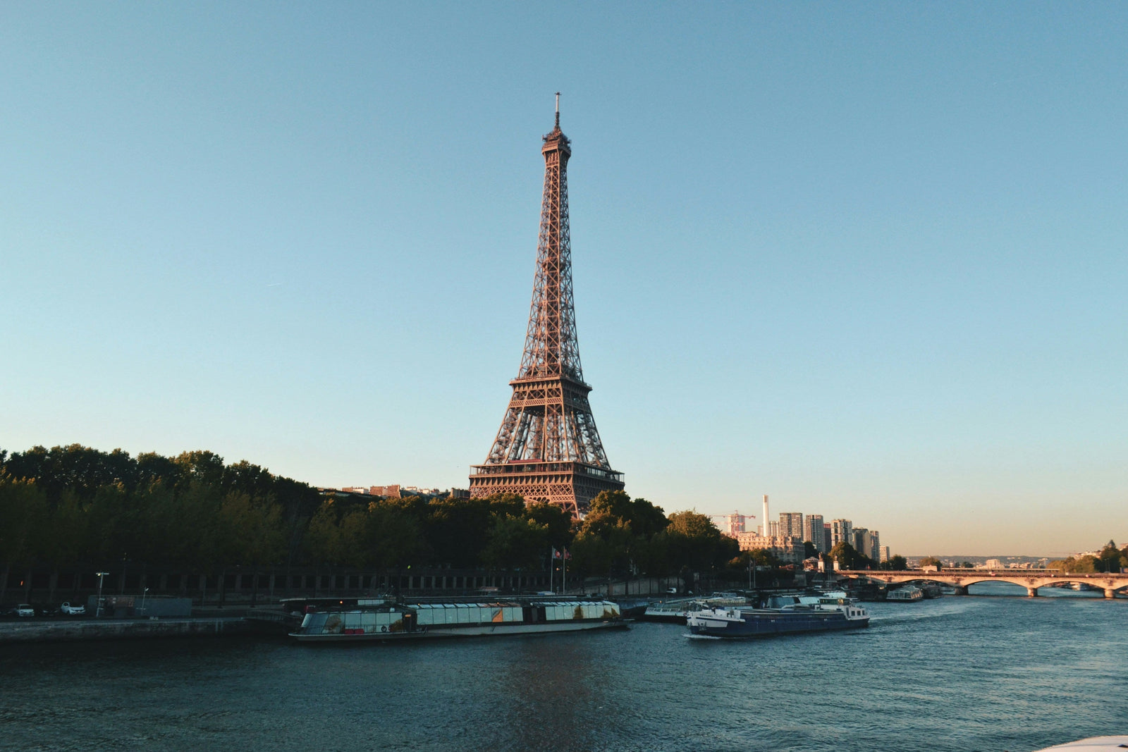 Eiffel Tower at sunset with boats on the Seine River and clear blue sky in Paris.