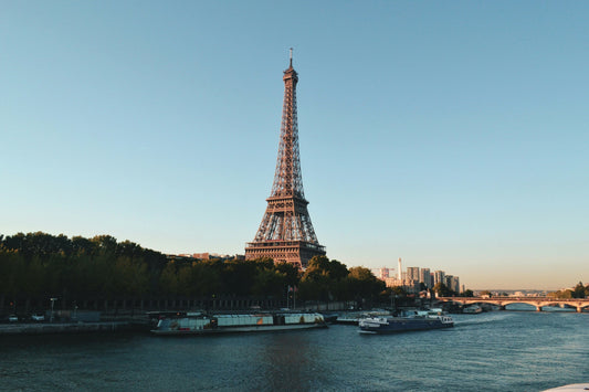 Eiffel Tower at sunset with boats on the Seine River and clear blue sky in Paris.
